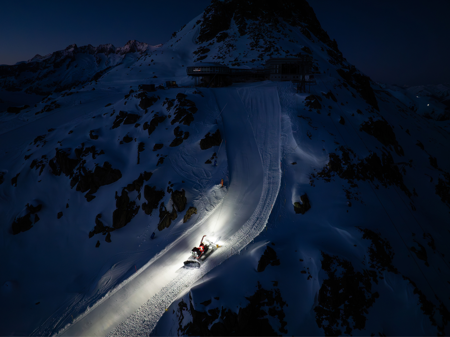 Luftaufnahme einer bei Nacht beleuchteten Piste im Gebirge