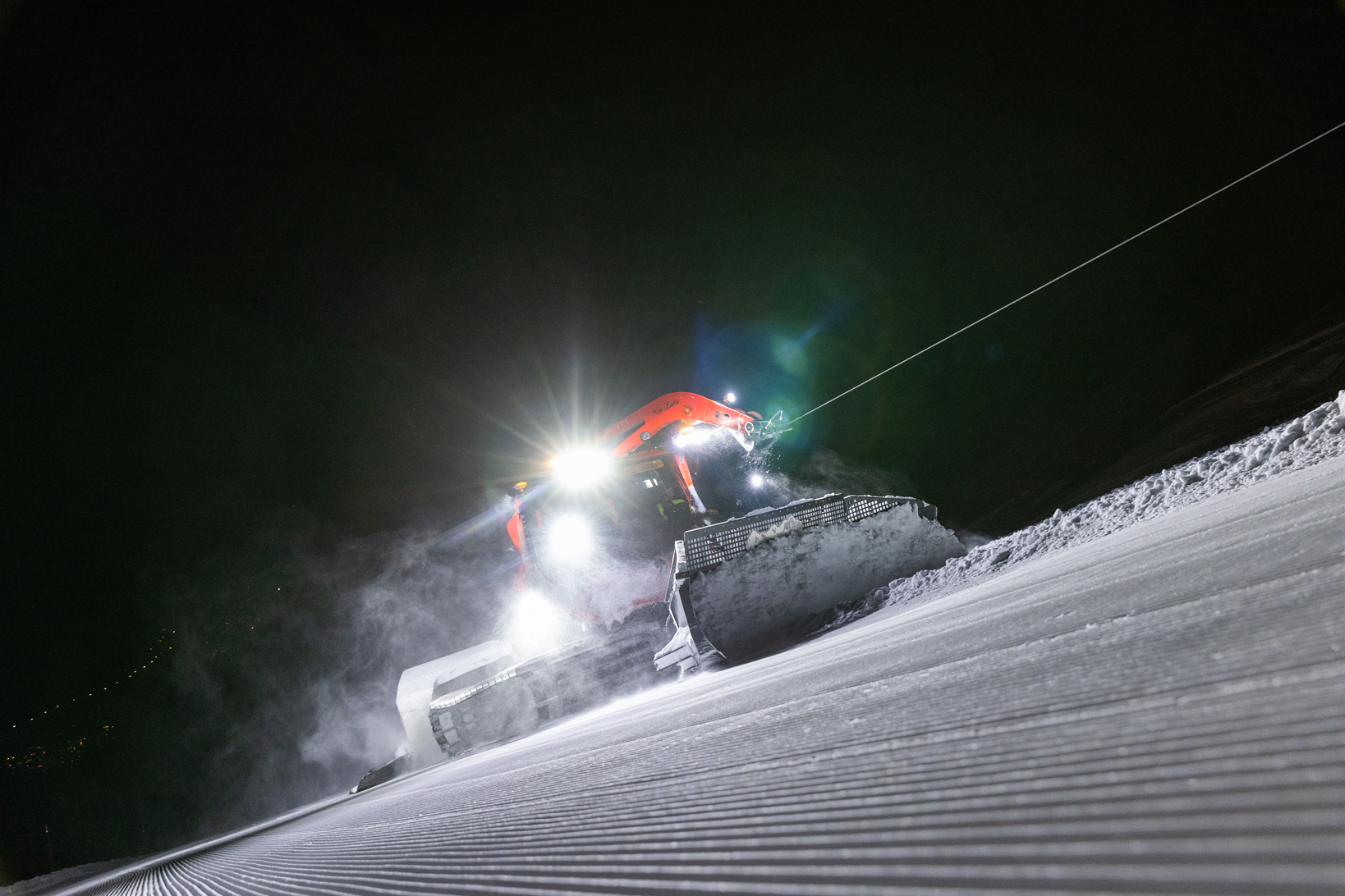 Pistenraupe bei Nacht mit Scheinwerfern auf der frisch gezogenen Piste
