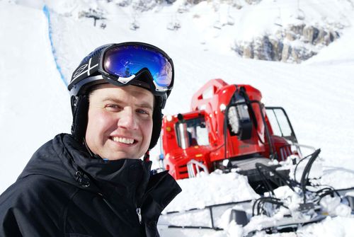 Teilnehmer mit Helm und Skibrille vor einer Pistenraupe